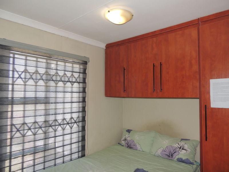 A bedroom featuring built-in wooden cupboards, a window with a security gate, and a ceiling light fixture.