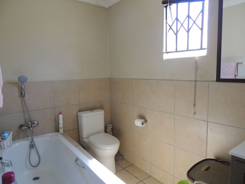 A functional bathroom featuring a bathtub with handheld shower, toilet, and neutral wall tiling with a window security gate.