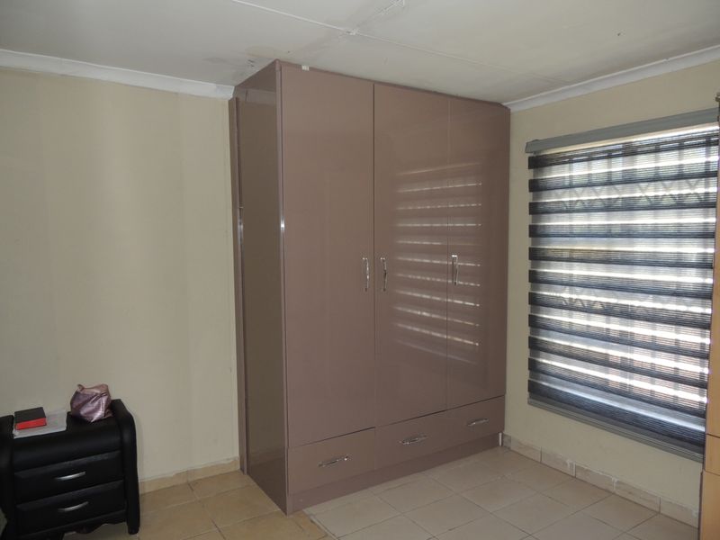 A bedroom featuring a modern built-in wardrobe, tiled flooring, and window blinds, with visible ceiling water staining requiring attention.