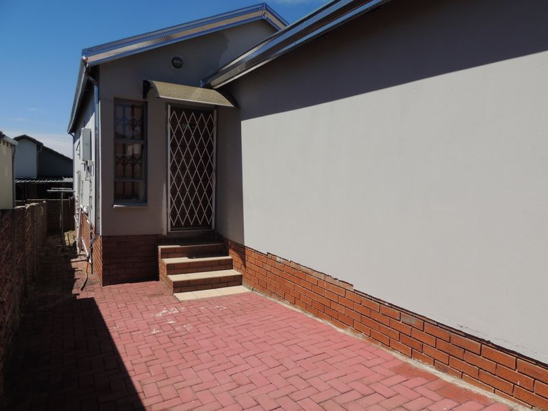 Rear exterior view showing a paved patio area, brick plinth detailing, and a secure entrance door with a protective awning.
