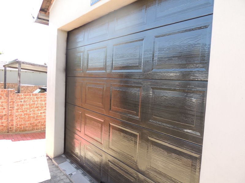A view of a dark brown wood-grain finish sectional garage door set within a residential exterior.