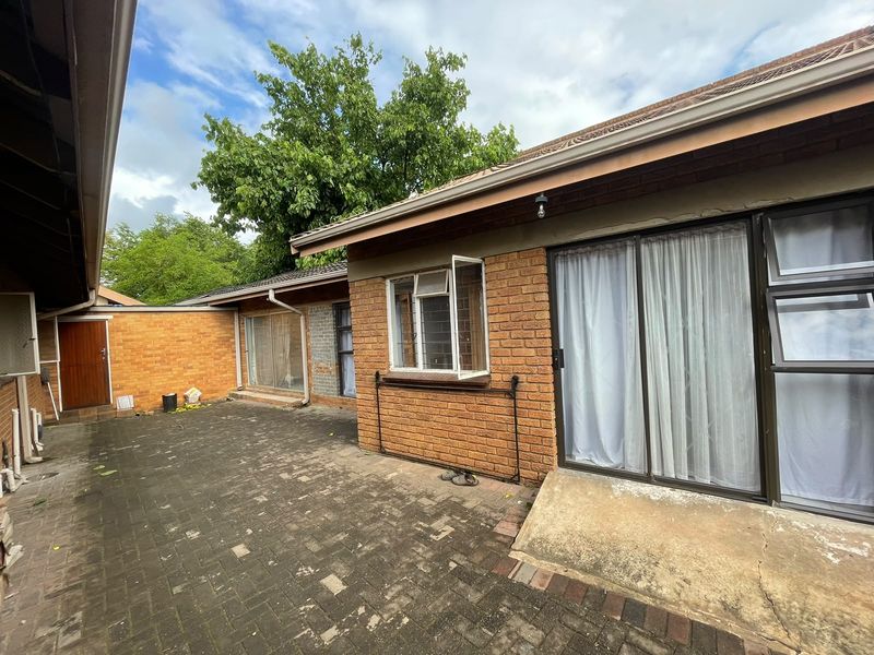 Rear exterior view of the property featuring a paved courtyard, brick facade, and sliding glass door access.