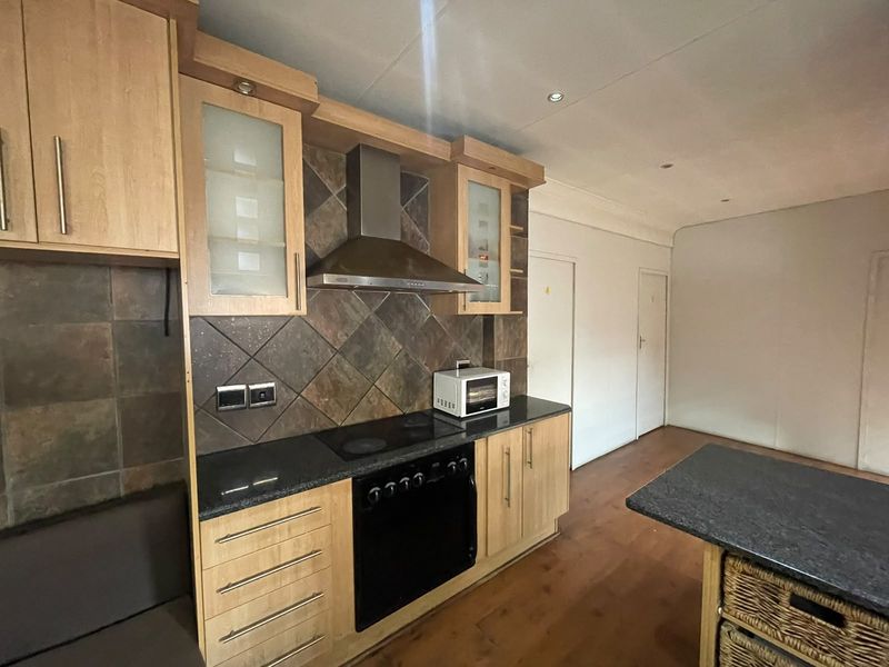 A functional kitchen featuring light wood cabinetry, dark stone countertops, a built-in oven with hob, and a tiled backsplash.