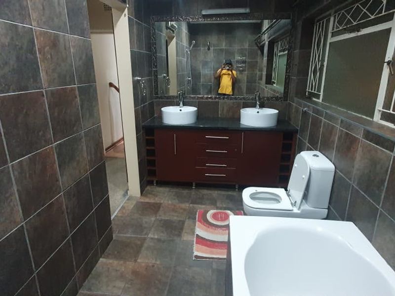 A spacious bathroom featuring a double vanity with vessel sinks, a bathtub, a toilet, and full-height wall tiling.