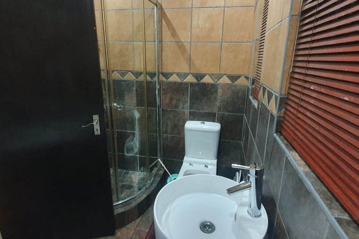 A compact bathroom featuring a corner shower enclosure, tiled walls, a modern vessel sink with chrome mixer, and wooden venetian blinds.