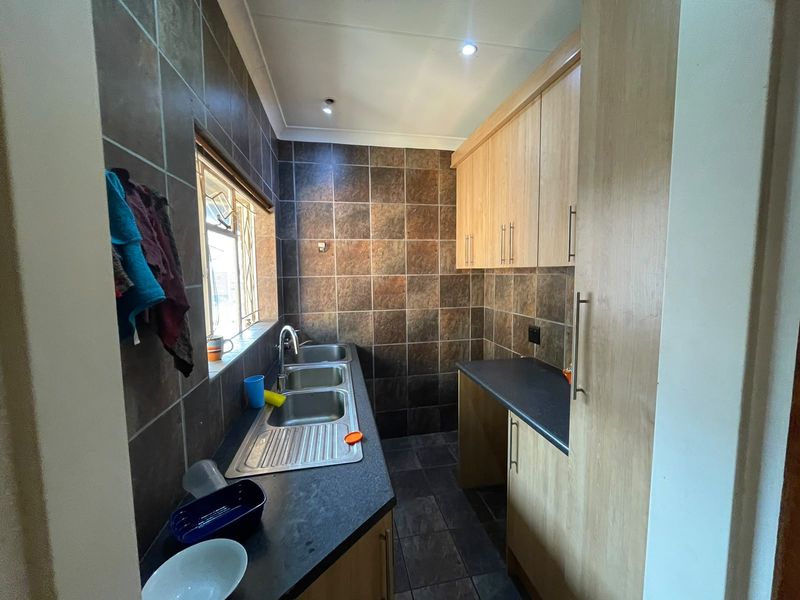 A functional scullery featuring a triple bowl stainless steel sink, ample laminate cabinetry, dark countertops, and full-height tiled splashbacks.