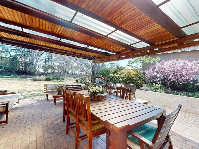 Spacious covered patio featuring a timber pergola with translucent roofing, overlooking a well-maintained garden with brick paving.
