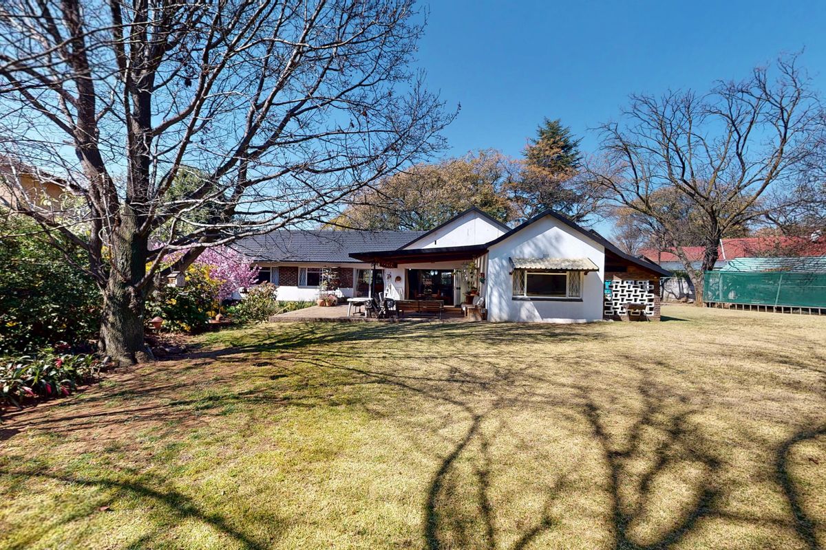 Rear view of the house featuring a spacious lawn, a covered patio area, and established garden trees.