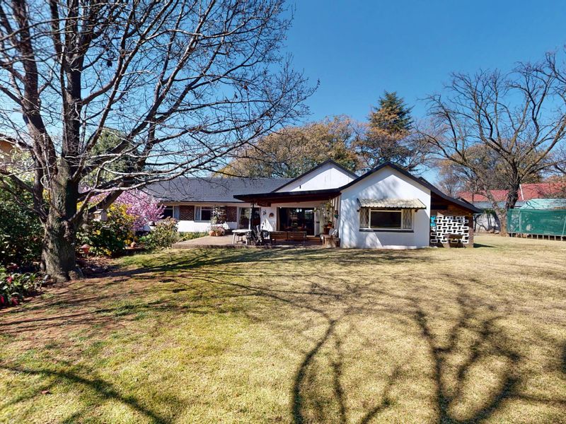 Rear view of the house featuring a spacious lawn, a covered patio area, and established garden trees.