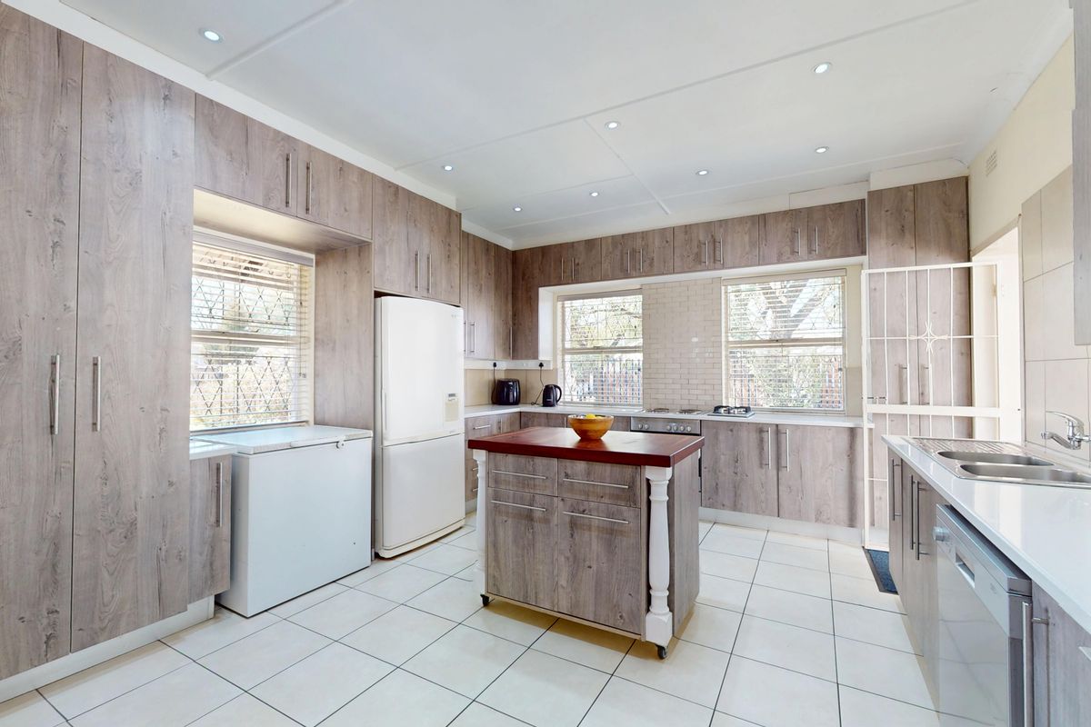 A well-maintained kitchen featuring wood-look cabinetry, a central island, tiled flooring, and integrated appliances, offering a functional and modern workspace.