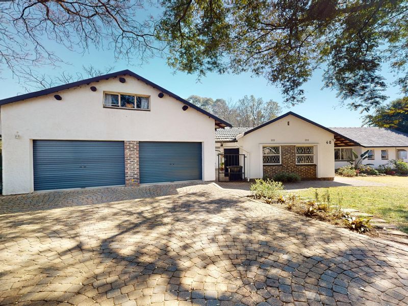 Front elevation of a residential property featuring a double garage, paved driveway, and established garden surroundings.