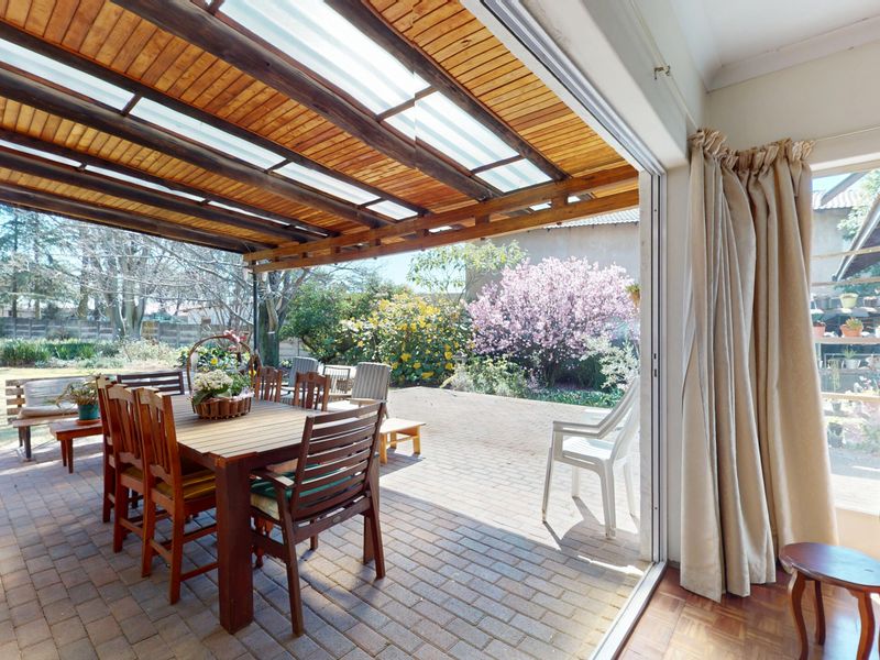 Covered outdoor patio featuring a timber-slatted pergola with translucent panels, brick paving, and seamless access to the garden through large sliding glass doors.
