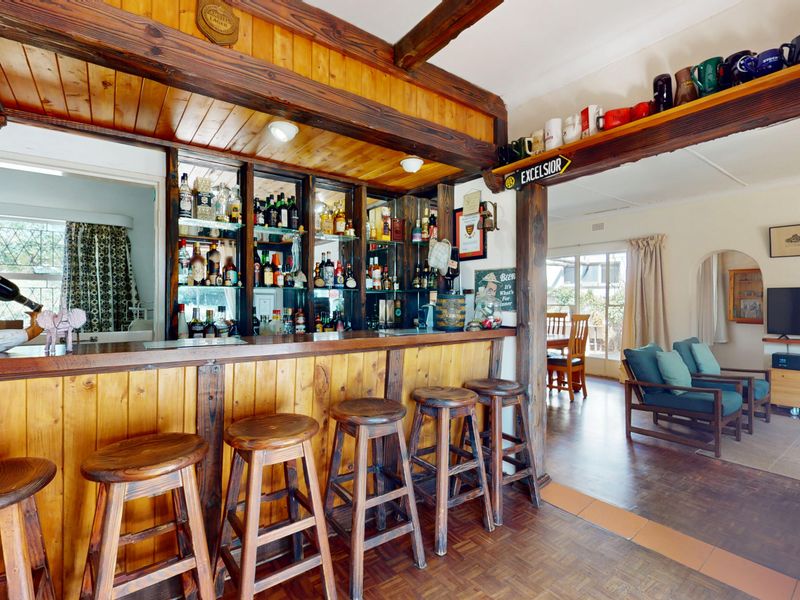 A dedicated bar area featuring built-in timber cabinetry, mirrored shelving, and exposed ceiling beams, seamlessly flowing into the adjacent living space.