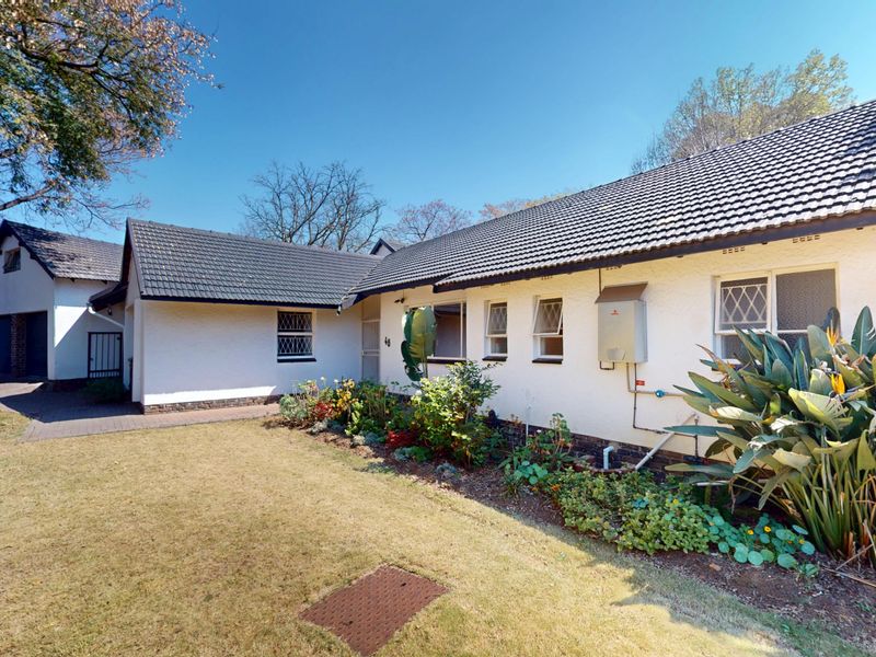 A well-maintained single-story home featuring a white stucco facade, tiled roof, diamond pane windows, and a neat front garden with a paved driveway.