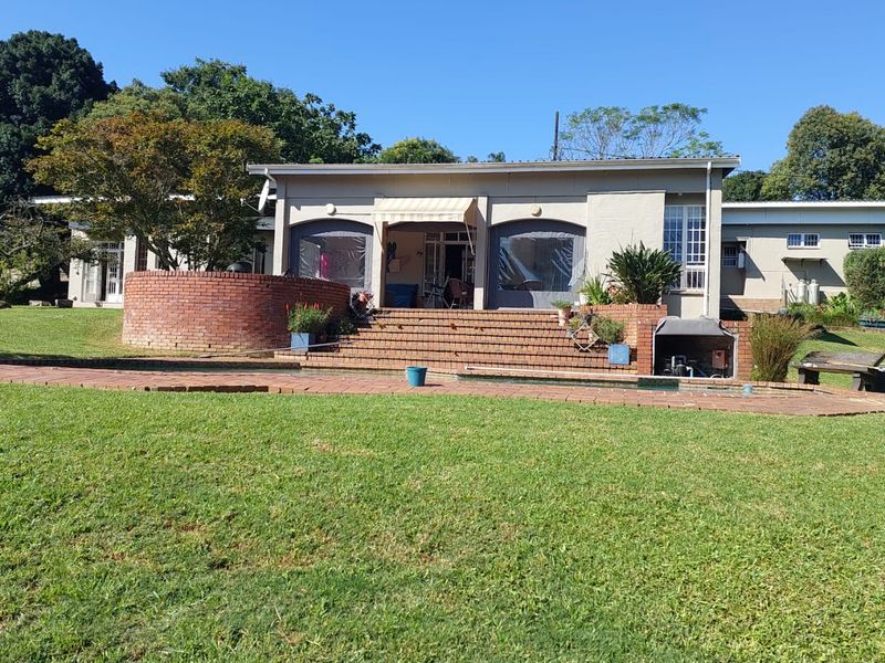 Rear view of the house featuring a spacious lawn, brick retaining wall, paved patio with retractable awning, and a swimming pool.