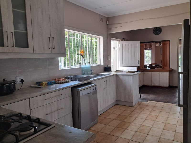 Functional kitchen featuring light-toned cabinetry, laminate countertops, gas hob, and tiled flooring, with an adjacent utility or dining area visible.