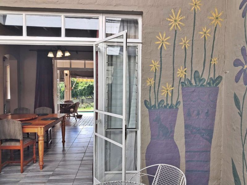 A covered patio area featuring tiled flooring and a glass door leading into the dining space, with decorative wall art on the exterior facade.