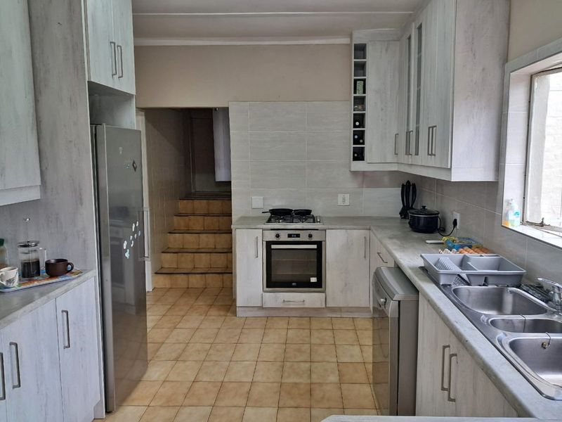 Functional kitchen featuring light-toned cabinetry, built-in oven with gas hob, double sink, and tiled flooring, with direct access to an adjacent staircase.