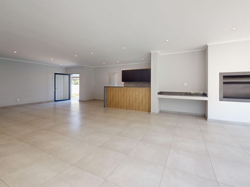 Spacious open-plan living area featuring neutral tiled flooring, recessed lighting, a built-in fireplace, and a modern bar counter, offering a versatile layout.