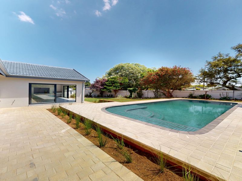 A well-maintained outdoor pool area featuring a paved deck, swimming pool, and direct access to the home through large sliding glass doors.