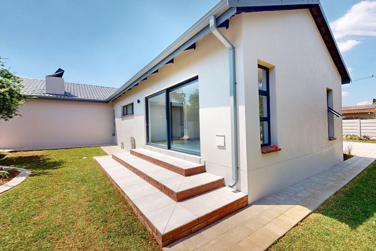 Rear view of the property featuring a well-maintained lawn, paved walkway, and tiled patio steps leading to a modern sliding glass door.