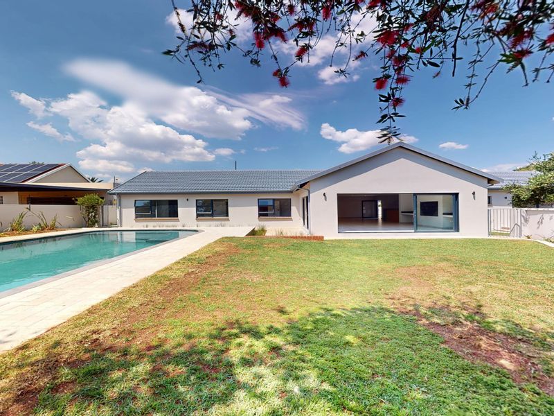 Rear view of the property featuring a well-maintained swimming pool, paved deck, and a spacious lawn leading to the main house structure.