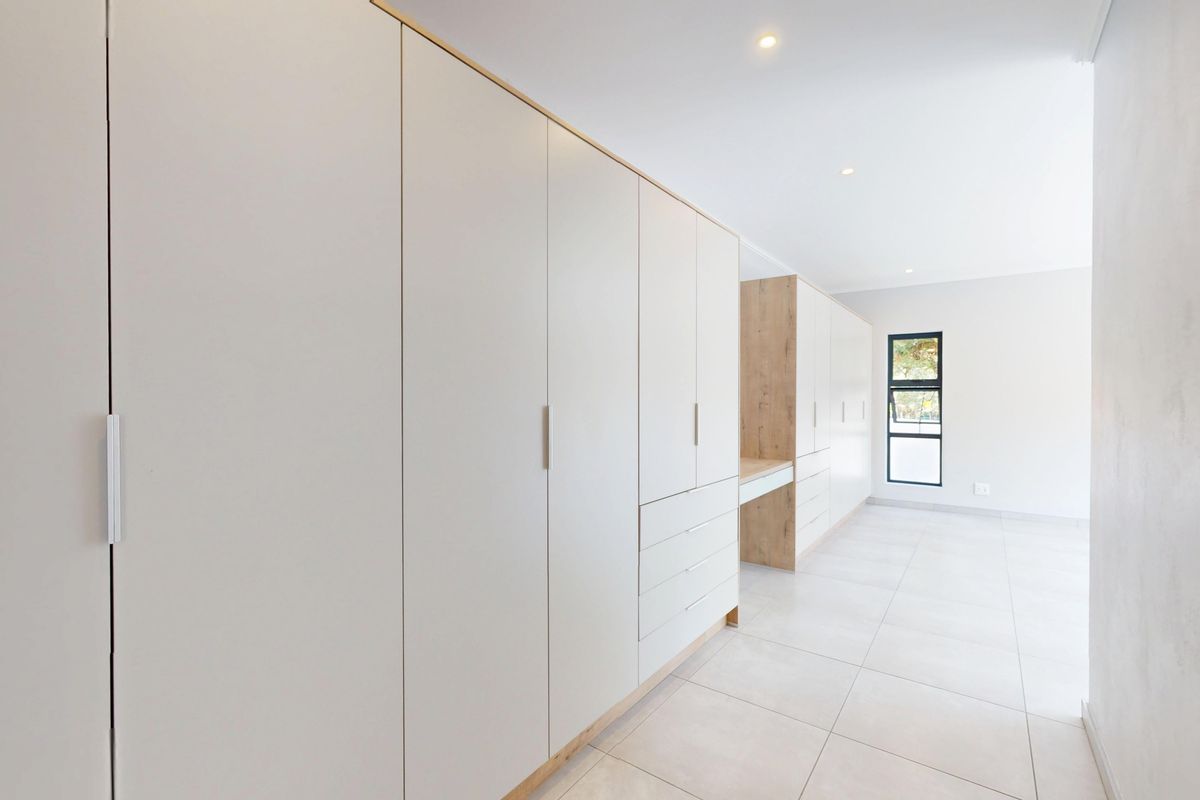 A bright, modern bedroom featuring extensive built-in cabinetry with an integrated desk, neutral tiled flooring, and clean, contemporary finishes.