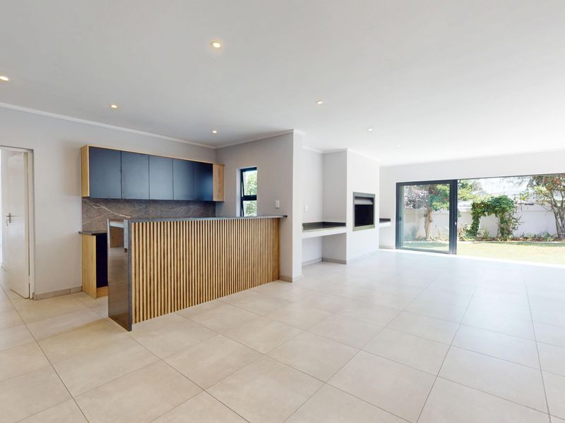 Spacious open-plan living area featuring modern cabinetry, a slatted timber breakfast bar, built-in fireplace, and large sliding doors opening to the garden.