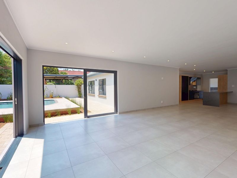 Spacious open-plan living area featuring large sliding doors leading to a pool area, with a modern kitchen island and neutral tiled flooring throughout.