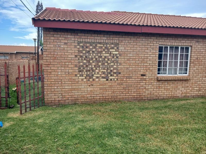 Rear exterior view of a brick house featuring a tiled roof, a window with security bars, and a visible brickwork repair patch on the wall.
