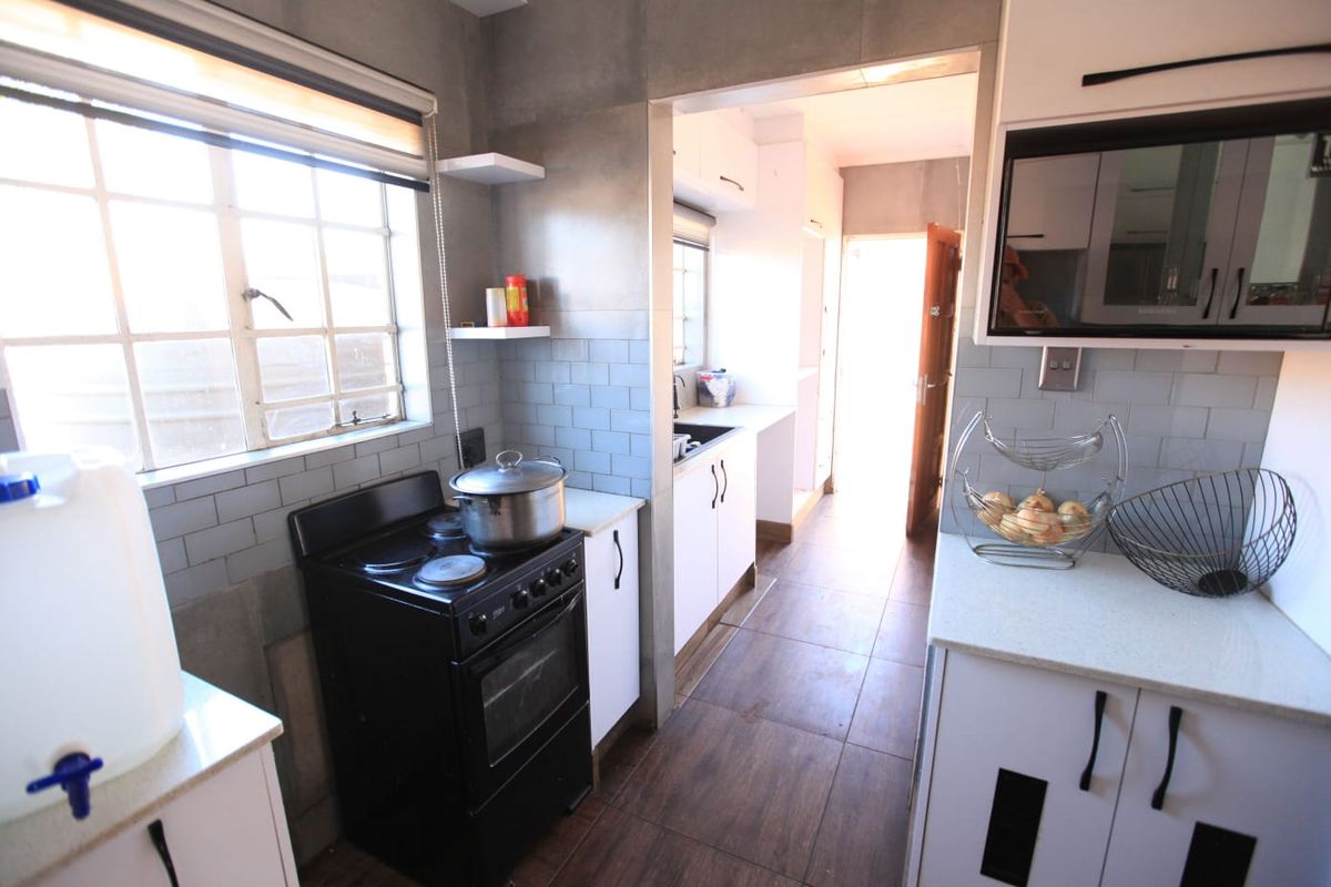 A functional kitchen featuring modern subway tile backsplashes, stone countertops, built-in cabinetry, and a freestanding stove, with an adjacent scullery area.