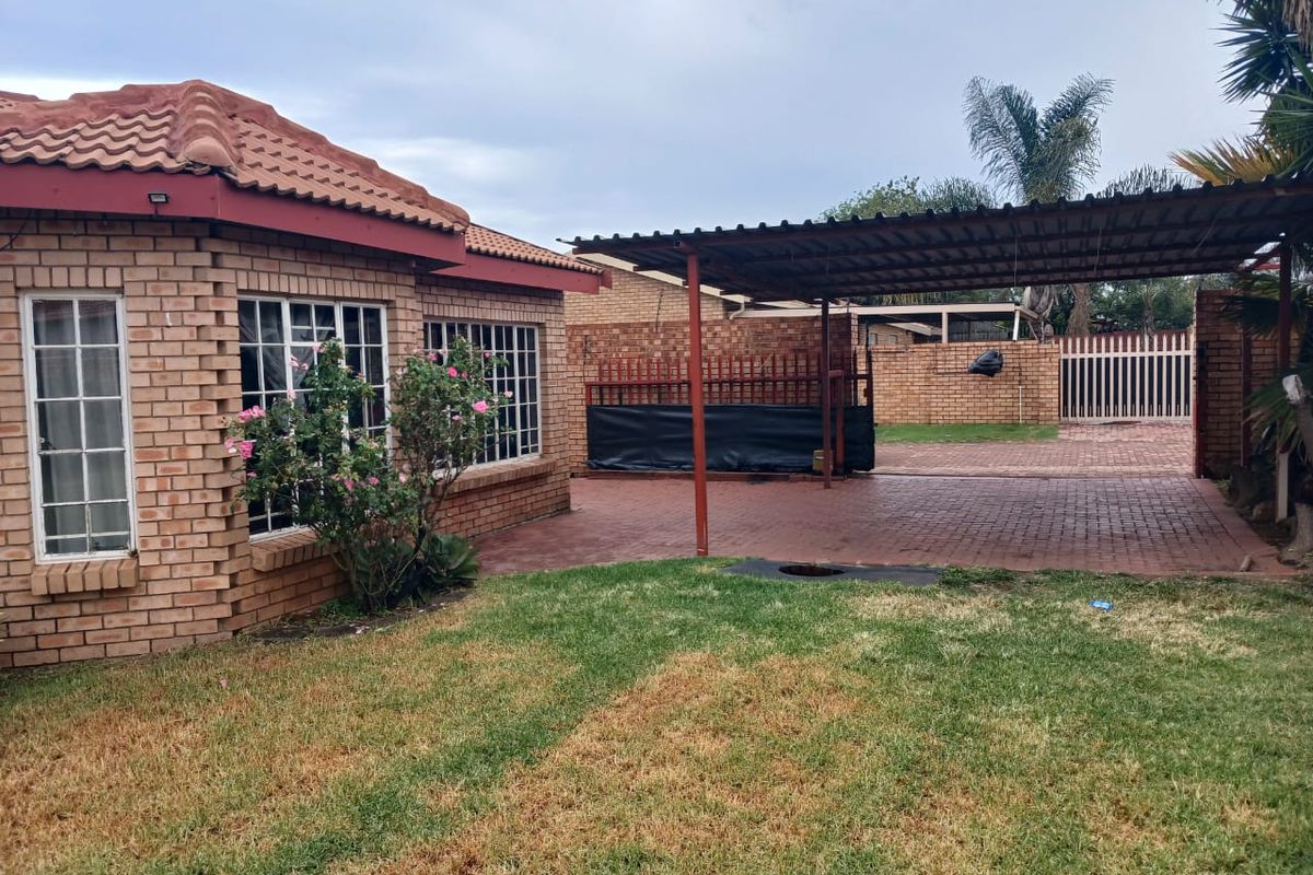 Rear exterior view of a face brick house featuring a paved driveway, covered carport, and a private garden area with boundary walling.