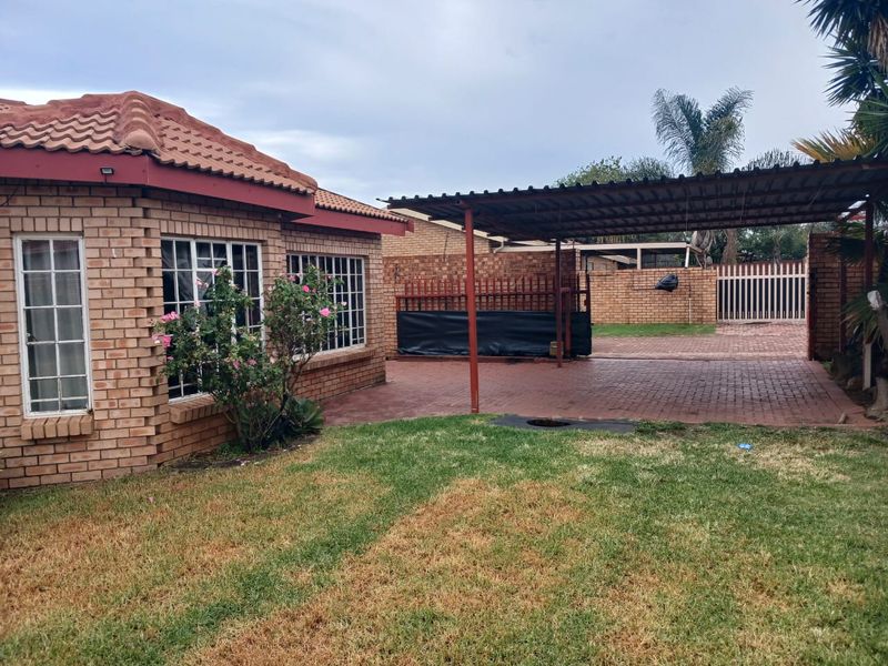Rear exterior view of a face brick house featuring a paved driveway, covered carport, and a private garden area with boundary walling.