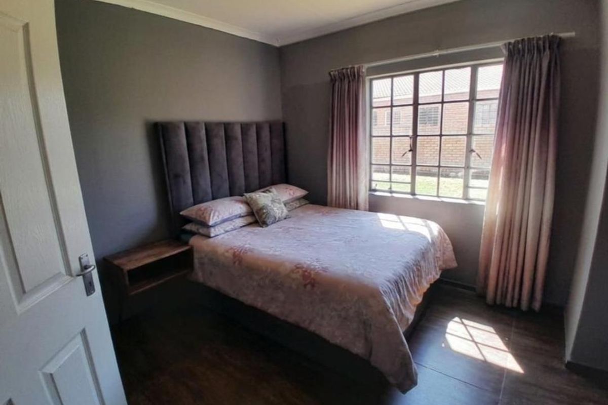 A cozy bedroom featuring dark grey walls, wood-look flooring, and a large steel-framed window that allows for natural light.