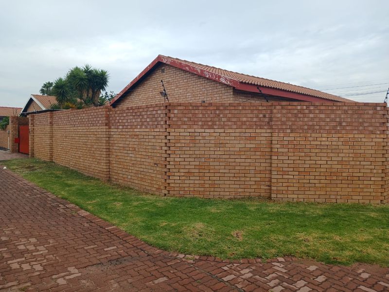 A view of the property's exterior featuring a secure face brick boundary wall, electric fencing, and a paved driveway approach.