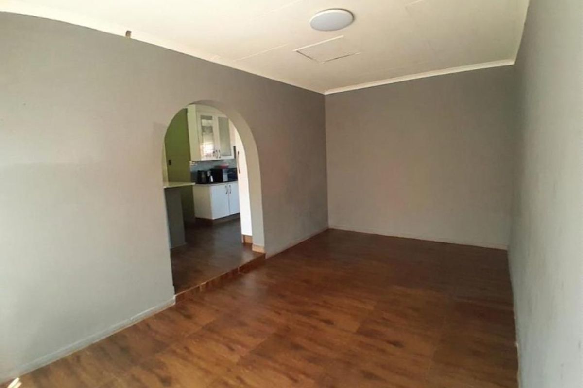 An empty living room featuring laminate flooring and an arched entryway leading into the kitchen area.