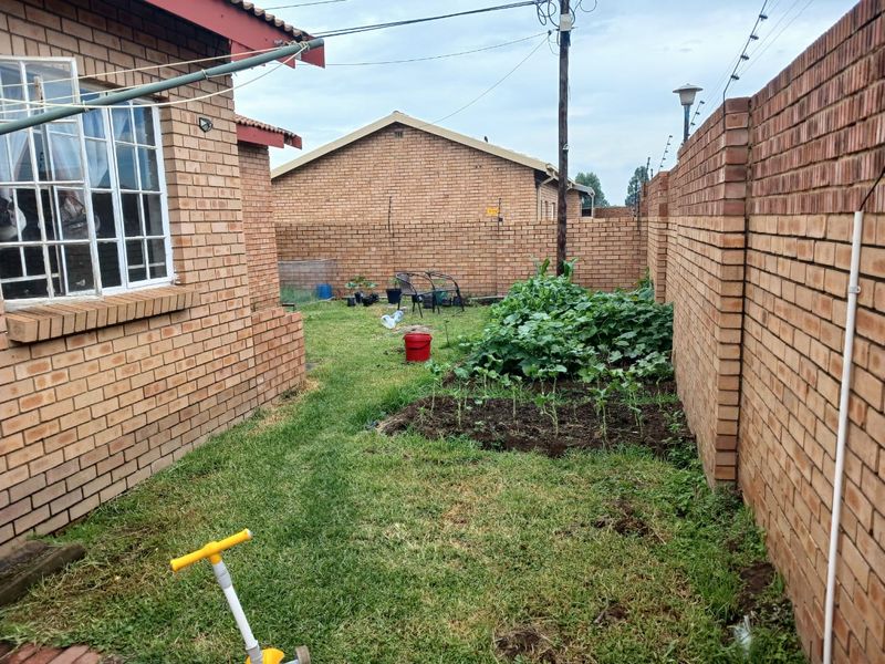 A rear garden area featuring face brick boundary walls, a small lawn, and a cultivated garden bed alongside the main house structure.