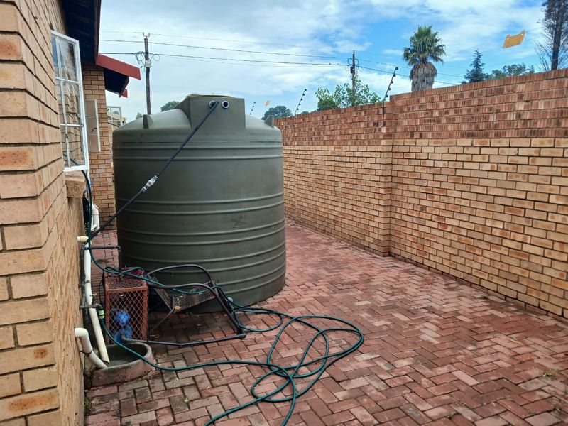 Rear courtyard area featuring a large water storage tank, brick boundary walls with electric fencing, and paved flooring.