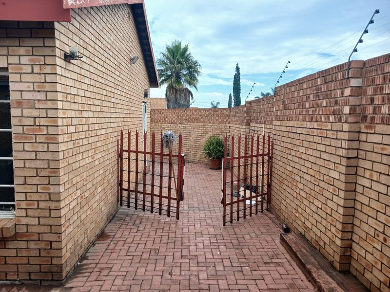 A private rear courtyard featuring face brick walls, paved flooring, and a secure metal gate with perimeter electric fencing.