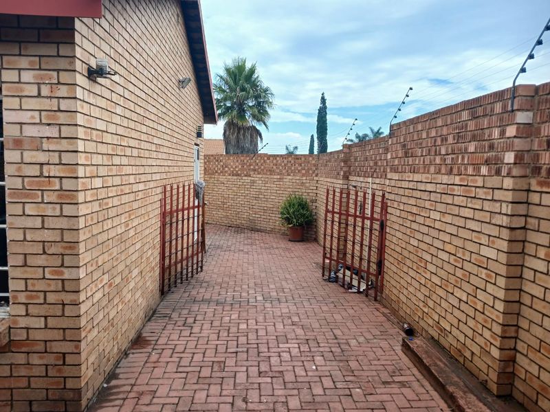 A side passage featuring brick paving, enclosed by high brick boundary walls with integrated electric fencing and a metal security gate.