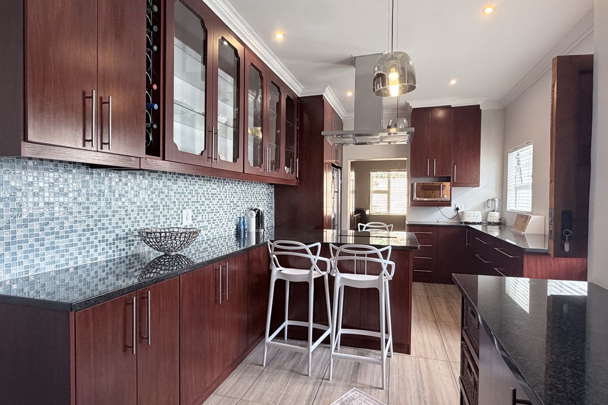 Modern kitchen featuring dark wood cabinetry, granite countertops, a mosaic tile backsplash, and a stainless steel extractor fan with integrated lighting.