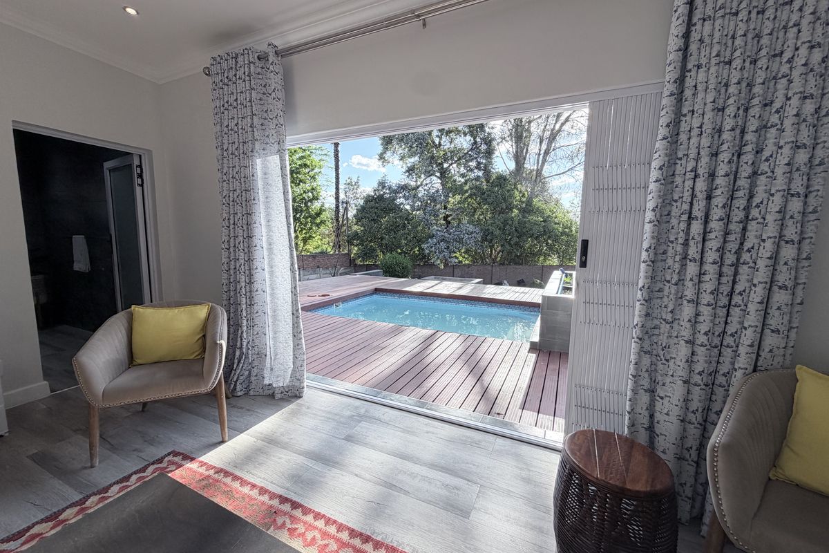 Bedroom featuring modern laminate flooring and large sliding glass doors that open directly onto a wooden deck with a swimming pool.
