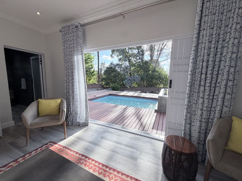 Bedroom featuring modern laminate flooring and large sliding glass doors that open directly onto a wooden deck with a swimming pool.
