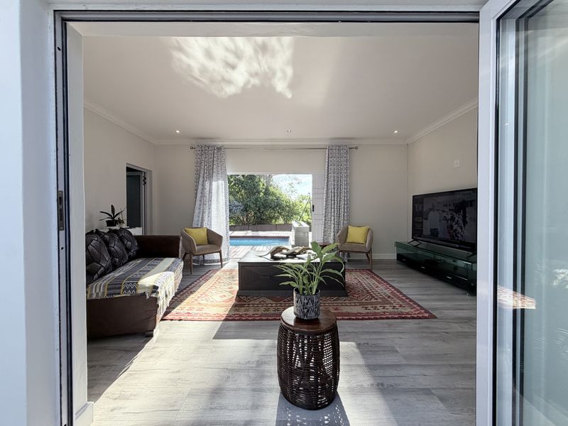 Bright and airy living room featuring modern laminate flooring, recessed lighting, and large sliding glass doors that open directly onto the pool area.