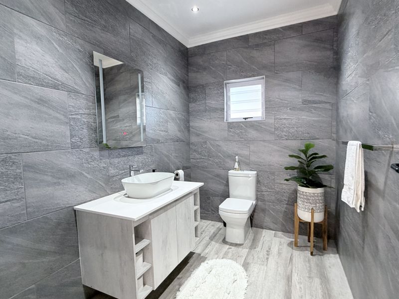 Modern bathroom featuring grey stone-look wall tiles, a contemporary vanity with vessel sink, and a white toilet.