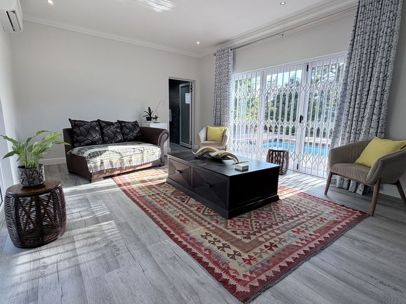 Bright living room featuring laminate flooring, recessed lighting, and large sliding glass doors with security gates providing direct access to the pool area.