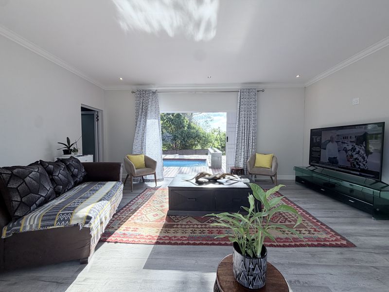 Spacious living room featuring modern laminate flooring, recessed lighting, and large sliding glass doors that open directly onto the outdoor pool area.