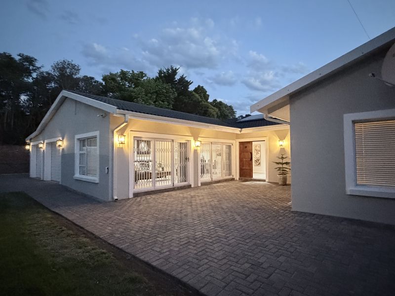 A well-maintained front exterior view of the house featuring a paved driveway, secure sliding doors, and exterior lighting at dusk.