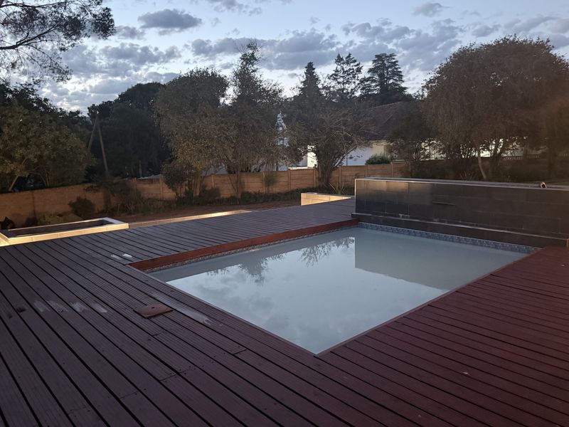 Outdoor pool area featuring a modern swimming pool surrounded by timber decking and a tiled water feature wall, set within a private garden.