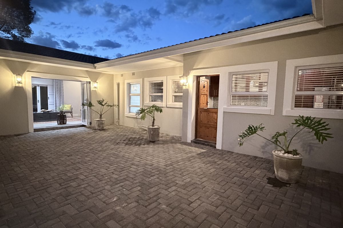 A well-maintained paved rear courtyard featuring a classic dutch door, modern sliding glass doors, and exterior wall lighting, creating a welcoming outdoor space.